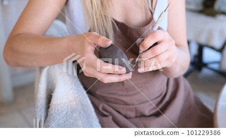 a woman processes a clay bowl with tools. 101229386