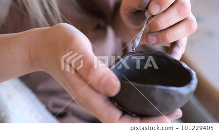 a woman processes a clay bowl with tools. 101229405