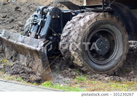Wheeled tractor with shovel clears ground on cloudy rainy day. Dirty bulldozer shovel close-up.. Wheeled tractor with shovel clears ground on cloudy rainy day. Dirty bulldozer shovel close-up.. 101230267