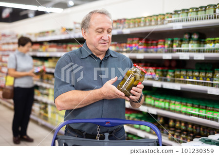 man chooses jar of canned cucumbers 101230359