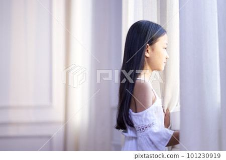9 year-old little asian girl standing in front of window looking out 101230919
