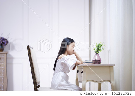 sad little asian girl with long black hair sitting at desk in her room thinking with hand on chin sad little asian girl with long black hair sitting at desk in her room thinking with hand on chin 101231722