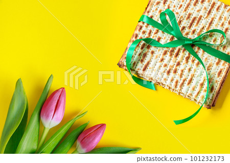 Traditional Jewish food matzo bread and pink tulips on yellow background. Happy Passover. Religious spring holiday Pesach. Copy space. Traditional Jewish food matzo bread and pink tulips on yellow background. Happy Passover. Religious spring holiday Pesach. Copy space. 101232173