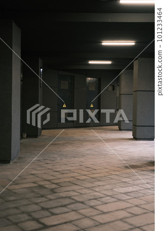 Long tunnel with columns in modern city architecture with low lights and grey colors with tile on the frloor and electricity shield room doors in front 101233464