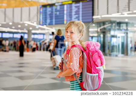 Little preschool girl at airport terminal. Happy child going on vacations by airplane. Smiling kid with passport and bag. 101234228