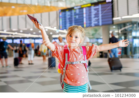 Little preschool girl at airport terminal. Happy child going on vacations by airplane. Smiling kid with passport and bag. 101234300