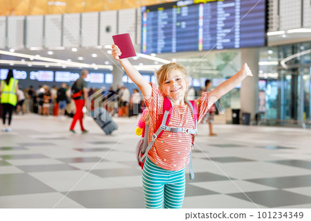 Little preschool girl at airport terminal. Happy child going on vacations by airplane. Smiling kid with passport and bag. 101234349