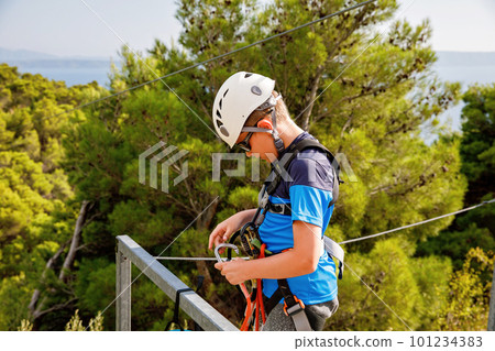 School boy preparing for zipline adventure. Happy active child put safety helmet on head. Summer fun with climbing in mountains. 101234383