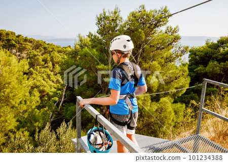 School boy preparing for zipline adventure. Happy active child put safety helmet on head. Summer fun with climbing in mountains. School boy preparing for zipline adventure. Happy active child put safety helmet on head. Summer fun with climbing in mountains. 101234388