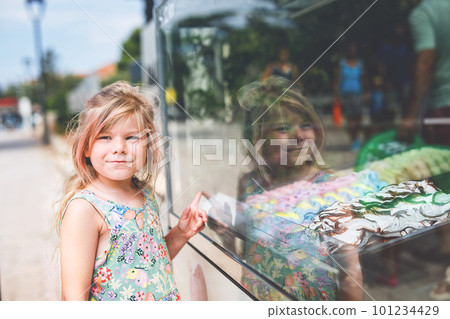 Happy preschool girl choosing and buying ice cream in outdoor stand cafe. Cute child looking at different sorts of icecream. Sweet summer dessert on family vacations. Summertime. Happy preschool girl choosing and buying ice cream in outdoor stand cafe. Cute child looking at different sorts of icecream. Sweet summer dessert on family vacations. Summertime. 101234429