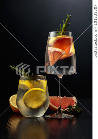 Gin tonic with ice, rosemary, lemon, and grapefruit on a black wooden table. 101235307