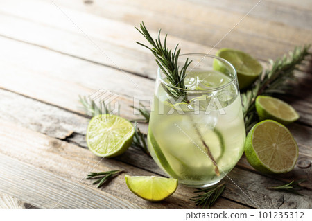 Gin tonic with ice, rosemary, and lime slices on an old wooden table. Gin tonic with ice, rosemary, and lime slices on an old wooden table. 101235312