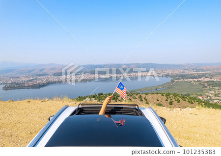 Woman holding Malaysia flag from the open car sunroof,  window driving along the serpentine road in the mountains. Top view. Concept 101235383