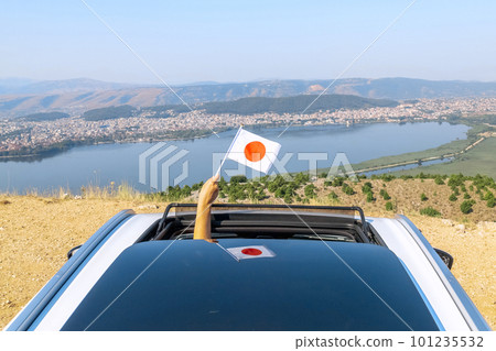Woman holding Japan flag from the open car sunroof, window driving along the serpentine road in the mountains. Top view. Concept Woman holding Japan flag from the open car sunroof, window driving along the serpentine road in the mountains. Top view. Concept 101235532