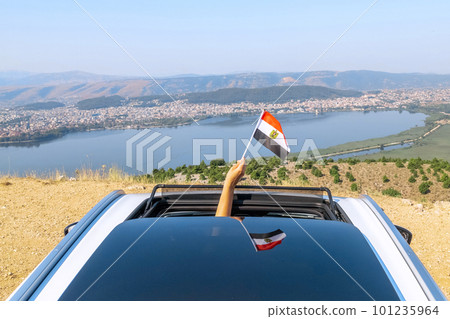 Woman holding Egypt flag from the open car sunroof,  window driving along the serpentine road in the mountains. Top view. Concept 101235964