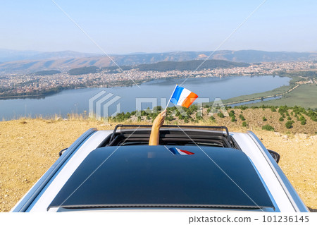 Woman holding France flag from the open car sunroof  window driving along the serpentine road in the mountains. Top view. Concept 101236145