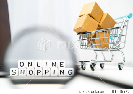 A magnifying glass is used to view cubes with words Online shopping while a toy shopping cart and boxes serve as the background. 101236572