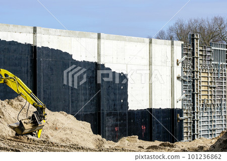 Concrete wall built using concrete formwork, partly covered with waterproofing sealant and earth 101236862