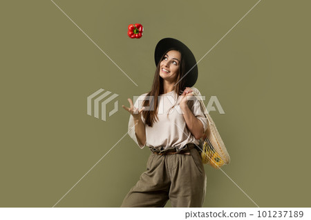 Young excited happy fun vegetarian woman 20s wear casual clothes and black hat hold net eco bag with vegetables after shopping in greengrocer and throw up a red pepper in air. 101237189
