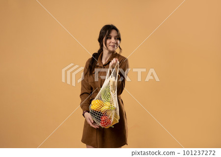 Zero waste concept. Young beautifull brunette woman holding reusable mesh shopping bags with vegetables, products. Eco friendly mesh shopper. Zero waste, plastic free concept. Zero waste concept. Young beautifull brunette woman holding reusable mesh shopping bags with vegetables, products. Eco friendly mesh shopper. Zero waste, plastic free concept. 101237272