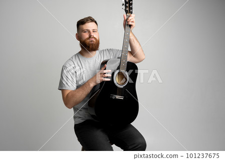 Handsome bearded brutal man musician holding a acoustic guitar on a shoulder. 101237675