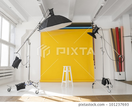 Yellow background roll with a white chair and two professional flash on a c-stands. Sunny daylight photo studio interior with set of professional equipment. Yellow background roll with a white chair and two professional flash on a c-stands. Sunny daylight photo studio interior with set of professional equipment. 101237693