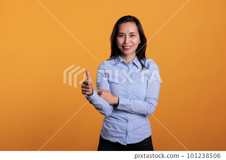 Smiling joyful asian woman giving thumbs up gesture, standing over yellow background. Successful brunette young adult showing okay and approval sign in studio. Approving symbol concept 101238506