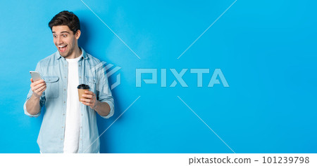 Man looking surprised at smartphone, drinking coffee, standing over blue background amazed Man looking surprised at smartphone, drinking coffee, standing over blue background amazed 101239798