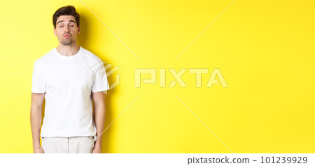 Image of lovely man close eyes and pucker lips, waiting for kiss, standing in white clothes against yellow background 101239929