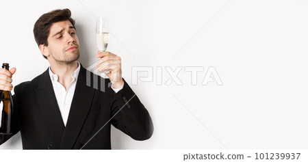 Close-up of attractive man in trendy suit, tasting champagne, looking at glass, standing against white background 101239937