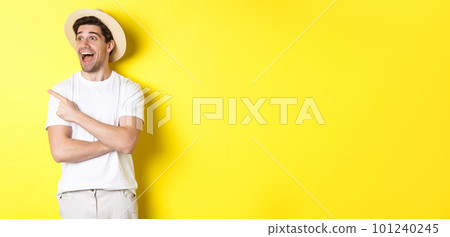 Concept of tourism and lifestyle. Excited handsome guy in straw hat checking out advertisement, pointing and looking at upper left corner logo, yellow background Concept of tourism and lifestyle. Excited handsome guy in straw hat checking out advertisement, pointing and looking at upper left corner logo, yellow background 101240245
