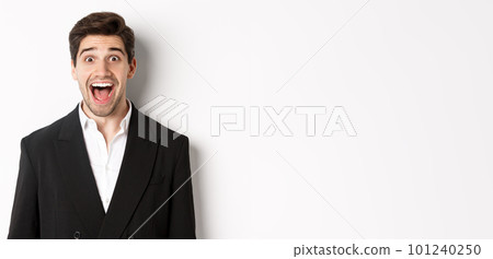 Close-up of attractive man in black suit, smiling amazed and looking at advertisement, standing over white background 101240250