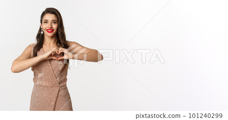 Celebration and party concept. Beautiful young woman in elegant dress showing heart sign, I love you gesture, express sympathy and smiling, white background 101240299