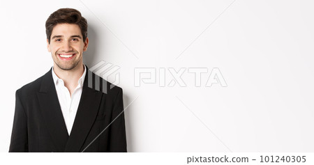 Close-up of handsome young businessman in trendy suit smiling, standing against white background 101240305