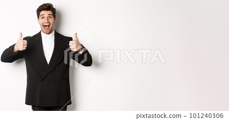 Concept of new year party, celebration and lifestyle. Portrait of amazed and pleased handsome man in black suit, showing thumbs-up, like product, approve something good, white background Concept of new year party, celebration and lifestyle. Portrait of amazed and pleased handsome man in black suit, showing thumbs-up, like product, approve something good, white background 101240306