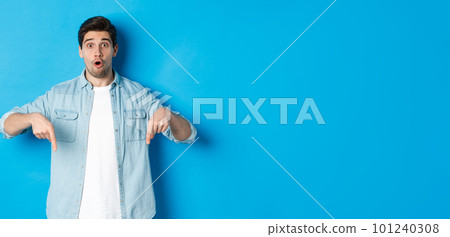 Surprised bearded adult man in casual outfit, pointing fingers down and looking startled, asking question about promotion, standing over blue background Surprised bearded adult man in casual outfit, pointing fingers down and looking startled, asking question about promotion, standing over blue background 101240308