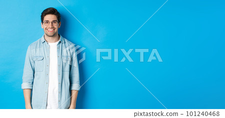 Young modern man in glasses and casual outfit standing against blue background, smiling happy at camera Young modern man in glasses and casual outfit standing against blue background, smiling happy at camera 101240468