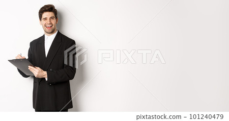 Image of handsome, successful boss in black suit, winking and smiling while signing documents, standing against white background Image of handsome, successful boss in black suit, winking and smiling while signing documents, standing against white background 101240479