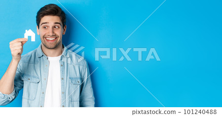 Real estate concept. Excited guy looking at small house model and smiling, renting apartment, standing over blue background Real estate concept. Excited guy looking at small house model and smiling, renting apartment, standing over blue background 101240488