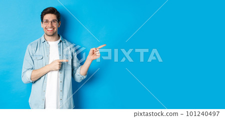 Handsome caucasian male model in glasses, pointing fingers right at your logo, showing copy space, standing over blue background Handsome caucasian male model in glasses, pointing fingers right at your logo, showing copy space, standing over blue background 101240497