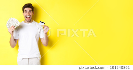 Excited man ready for black friday shopping, holding money and credit card, standing over yellow background Excited man ready for black friday shopping, holding money and credit card, standing over yellow background 101240861