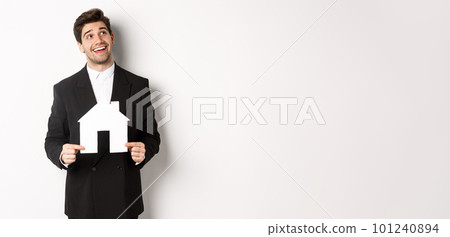 Portrait of handsome man in suit searching for home, holding paper house and looking at upper right corner dreamy, standing over white background Portrait of handsome man in suit searching for home, holding paper house and looking at upper right corner dreamy, standing over white background 101240894