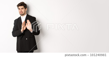 Image of stylish handsome man in black suit, cringe from something embarrassing, declining offer and showing stop gesture, standing against white background Image of stylish handsome man in black suit, cringe from something embarrassing, declining offer and showing stop gesture, standing against white background 101240981