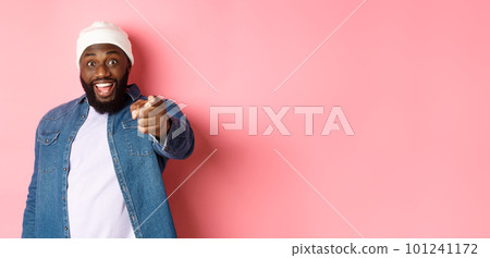 Happy african-american hipster man pointing finger at camera, need you, smiling excited, standing over pink background 101241172