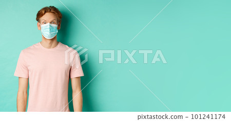 Covid-19, social distancing and quarantine concept. Young man raising eyebrows and looking surprised, wearing face mask during pandemic, standing over mint background Covid-19, social distancing and quarantine concept. Young man raising eyebrows and looking surprised, wearing face mask during pandemic, standing over mint background 101241174