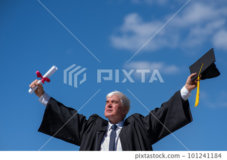 Elderly male graduate rejoices in receiving a diploma against a blue sky.  101241184