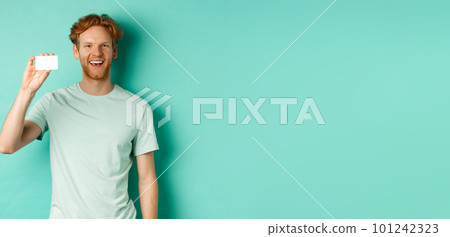 Shopping concept. Cheerful young man in t-shirt showing plastic credit card and smiling, standing over mint background 101242323