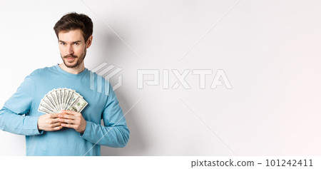 Confident bearded man smiling, showing dollars and looking at camera. Handsome guy holding money on white background 101242411