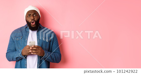 Technology and online shopping concept. Confused and disappointed african-american man complaining, holding mobile phone and staring at camera Technology and online shopping concept. Confused and disappointed african-american man complaining, holding mobile phone and staring at camera 101242922