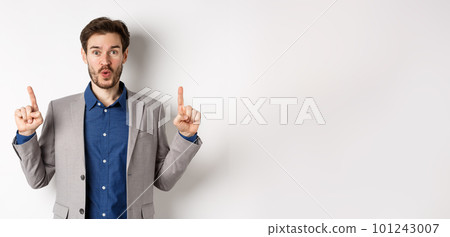 Excited businessman in suit say wow and smiling amused, pointing fingers up at good deal, standing against white background Excited businessman in suit say wow and smiling amused, pointing fingers up at good deal, standing against white background 101243007